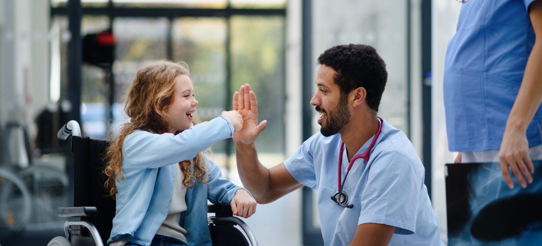 Young multiracial doctor having fun with little girl on a wheelchair.